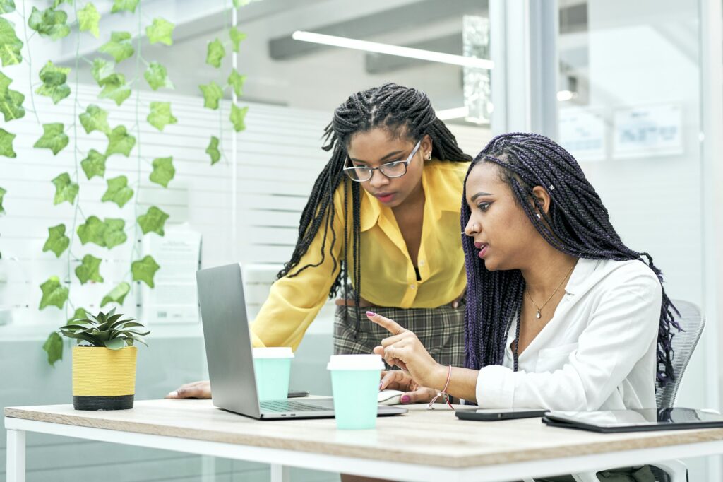 Two young black women reviewing analytical data on various electronic devices.