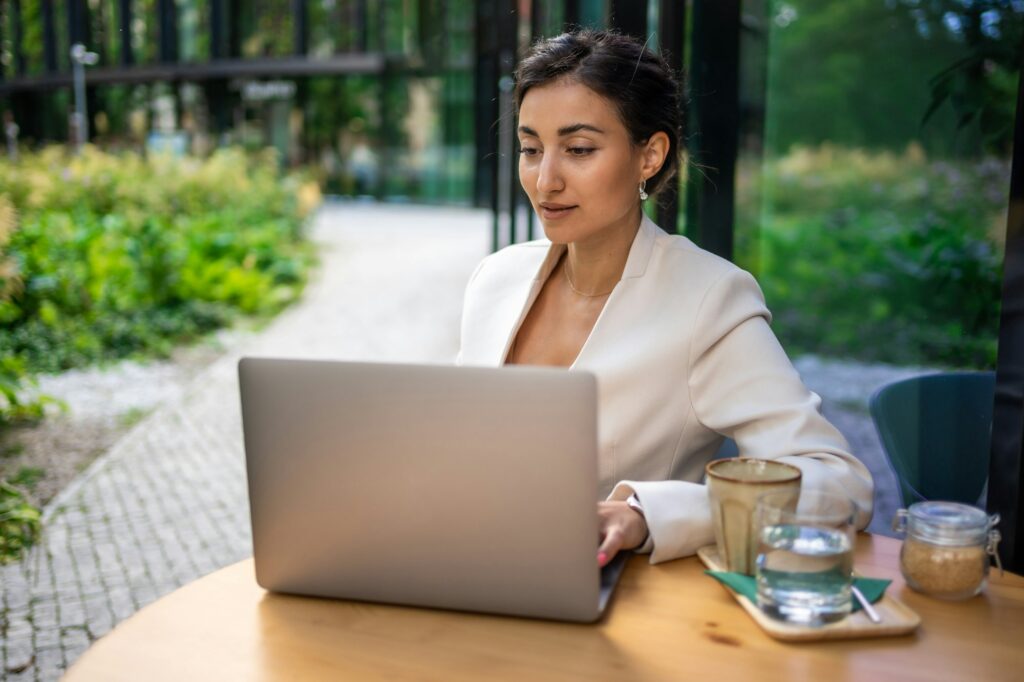 Young smiling brunette business woman in stylish smart dress working on laptop in cafe at street of